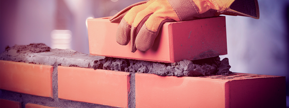 A person wearing gloves carefully arranges bricks on a brick wall, showcasing the importance of building trust in brand-customer relationships.